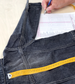 dos d'une veste en jean sur une table avec un mètre ruban pour effectuer une prise de mesure ainsi qu'un barème de mesure et une main pour noter la mesure - mises au point des produits